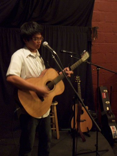 A photo of a person playing guitar standing in front of a mic