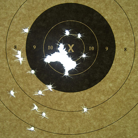 A target with several bullet holes in it. One main grouping in the lower left of the 10 ring and other holes scattered below